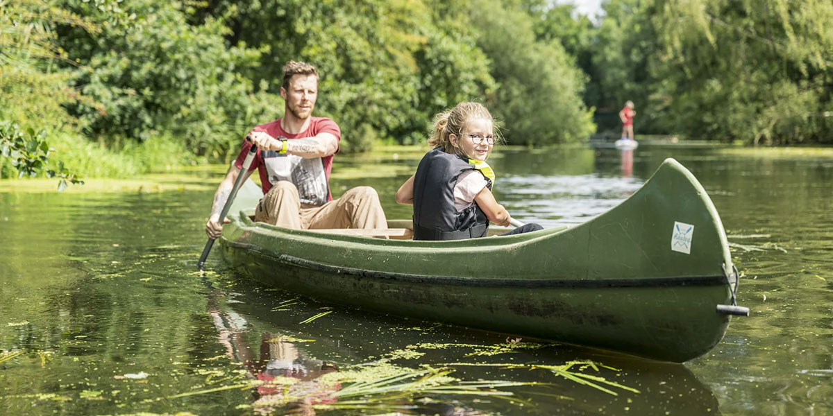 Ein Mann und ein Kind paddeln in einem grünen Kanu auf einem Fluss